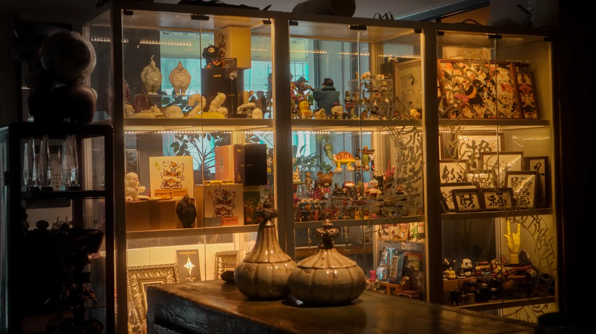 Curated art collection display cabinet at Lei Shi Tattoo — sculptures, paintings, and collectibles in warm gallery lighting